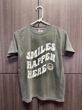 Load image into Gallery viewer, Gray t-shirt with 'Smiles Happen Here' text on a wooden background